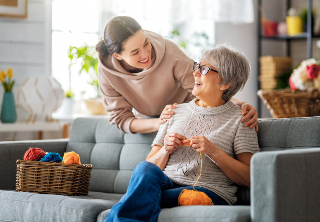 Beautiful mother and daughter are talking and smiling while sitting on couch at home.
