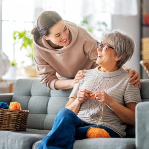 Beautiful mother and daughter are talking and smiling while sitting on couch at home.